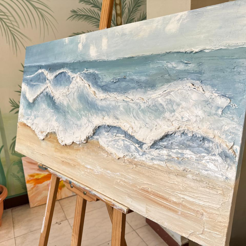 Oil painting of a beach scene on an easel with a blurred indoor background
