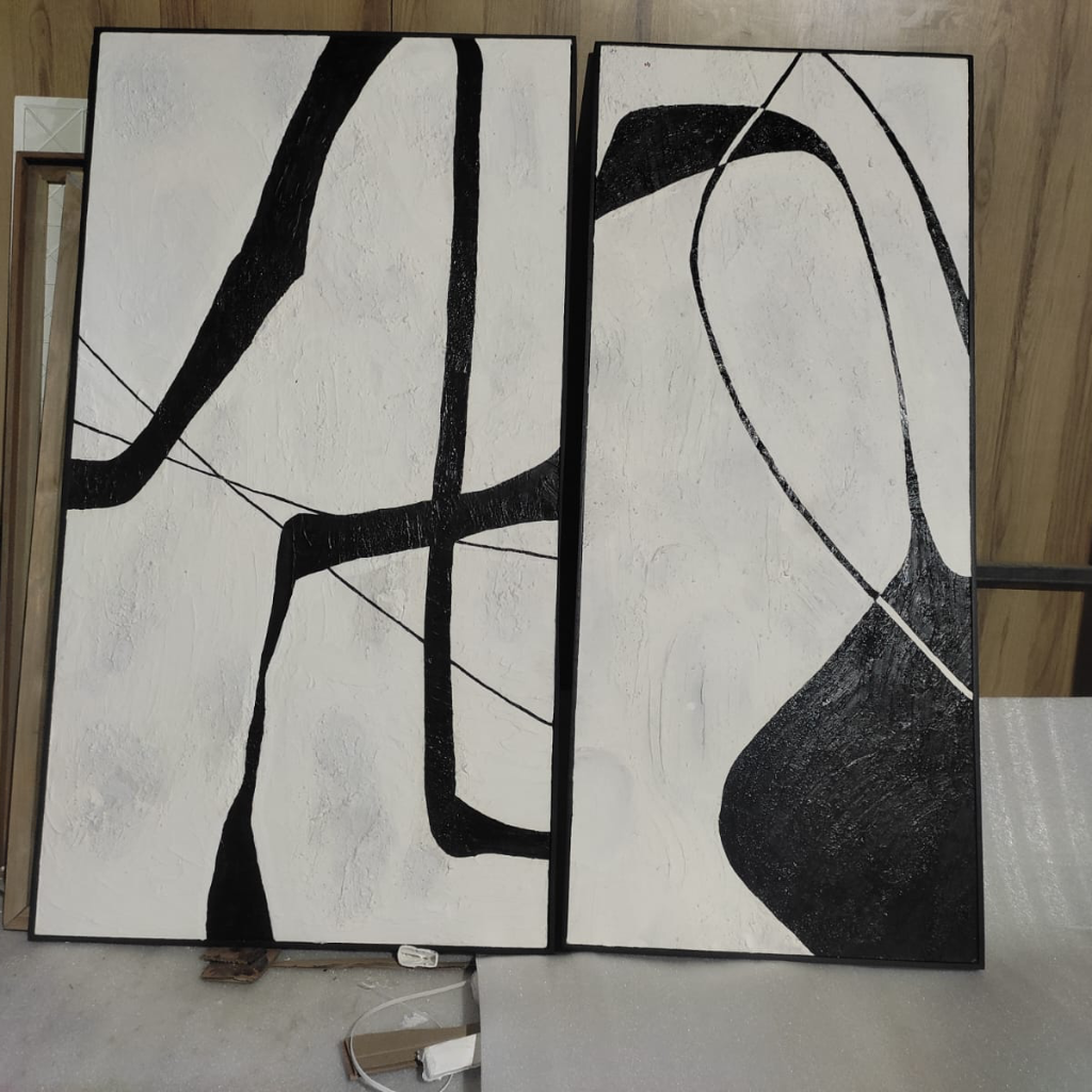Two abstract black and white artworks on a wooden floor.